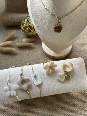 Sélection de bijoux artisanaux Nohulé Création sur présentoirs : collier avec pendentif fleur marron, bracelets fins avec breloques fleurs et géométriques, bague fleur blanche et bague d'oreille dorée.