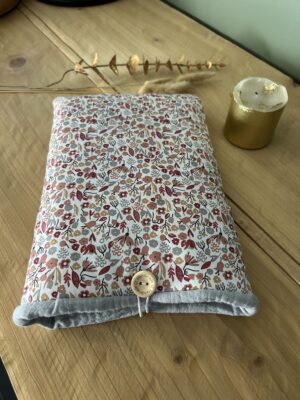 Pochette à livre artisanale matelassée Nohulé Création au motif fleuri gris et rouge, fermée par un bouton en bois sur une table.
