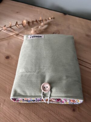 Broché velours vert amande Pochette à livre artisanale matelassée Nohulé Création au motif vert amande, fermée par un bouton en bois sur une table.