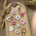 Sélection de pampilles artisanales (fleurs, cœur, carré) et anneaux créoles dorés et argentés pour boucles d'oreilles interchangeables Nohulé Création sur un plateau en bois.