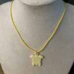 Collier ras de cou avec cordon de couleur jaune et pendentif artisanal en forme de petite tortue jaune clair Nohulé Création présenté sur un buste d'exposition blanc.