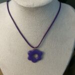Collier ras de cou avec cordon de couleur violet foncé et pendentif artisanal en forme de petite fleur violette assortie Nohulé Création présenté sur un buste d'exposition blanc.